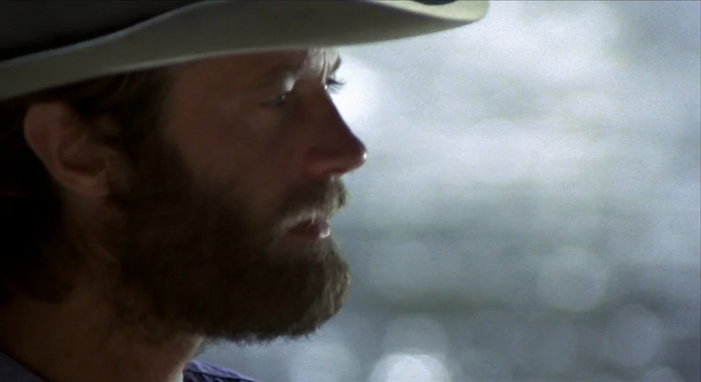 The Hired Hand (1971) movie still: closeup — A man in a cowboy hat is seen in close profile against a bright background. He looks ahead with a…