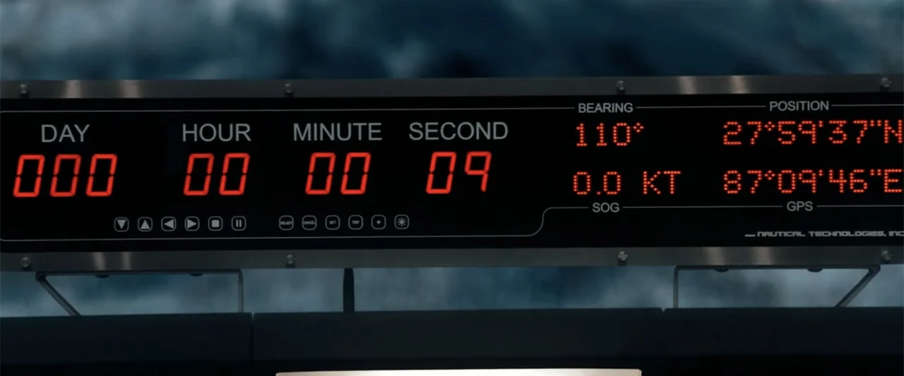 2012 (2009) movie still: closeup — A digital nautical technology console displays active red numerical data and GPS coordinates. The screen shows a…