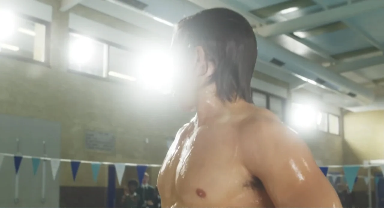 How to Date Billy Walsh (2024) movie still: medium — A high-ceilinged indoor facility features blue pennants stretched across a pool deck…