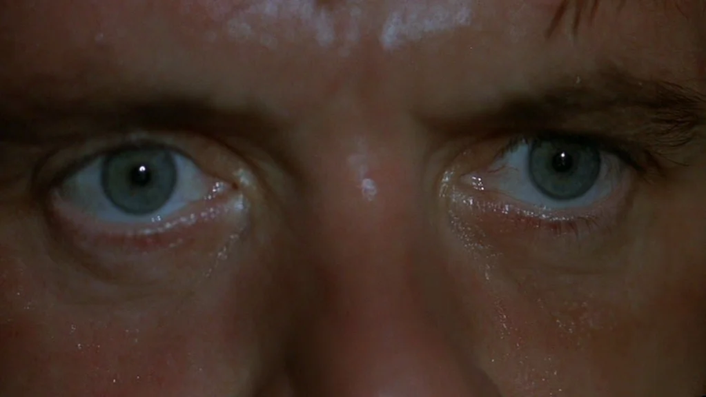 Magic (1978) movie still: closeup — A dark environment provides the background for this tight focus on a man's face. The subject stares ahead with…