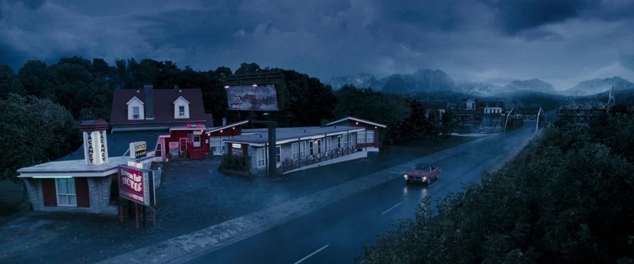 Dead Silence (2007) movie still: establishing — A dark, wet roadside at night shows a motel with a glowing vacancy sign. A single red car travels…