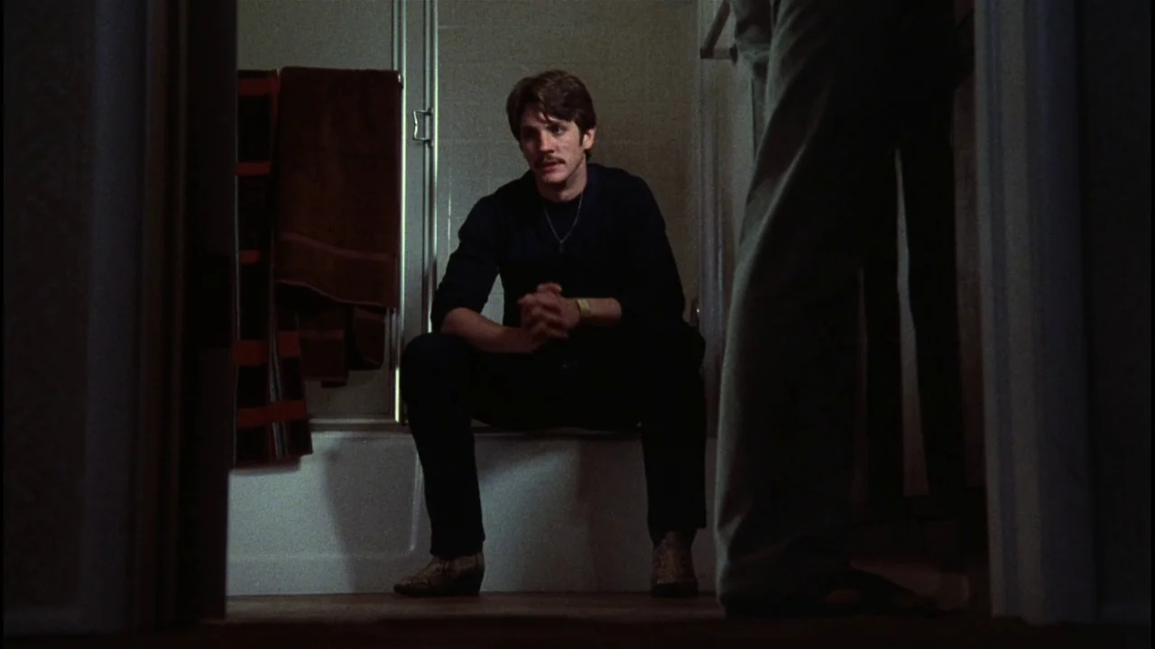 Star 80 (1983) movie still: medium — A dimly lit residential bathroom with a white bathtub and towels hanging nearby. A man with a mustache sits on…