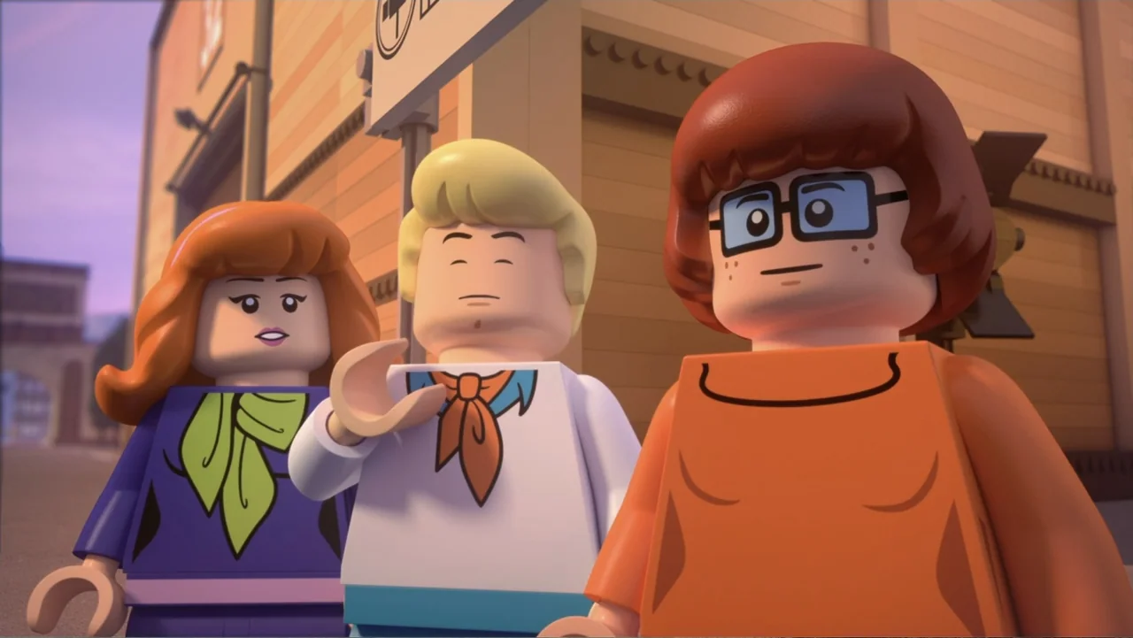 LEGO Scooby-Doo! Haunted Hollywood (2016) movie still: medium — Three animated lego-style characters stand in a town square during golden hour. The…