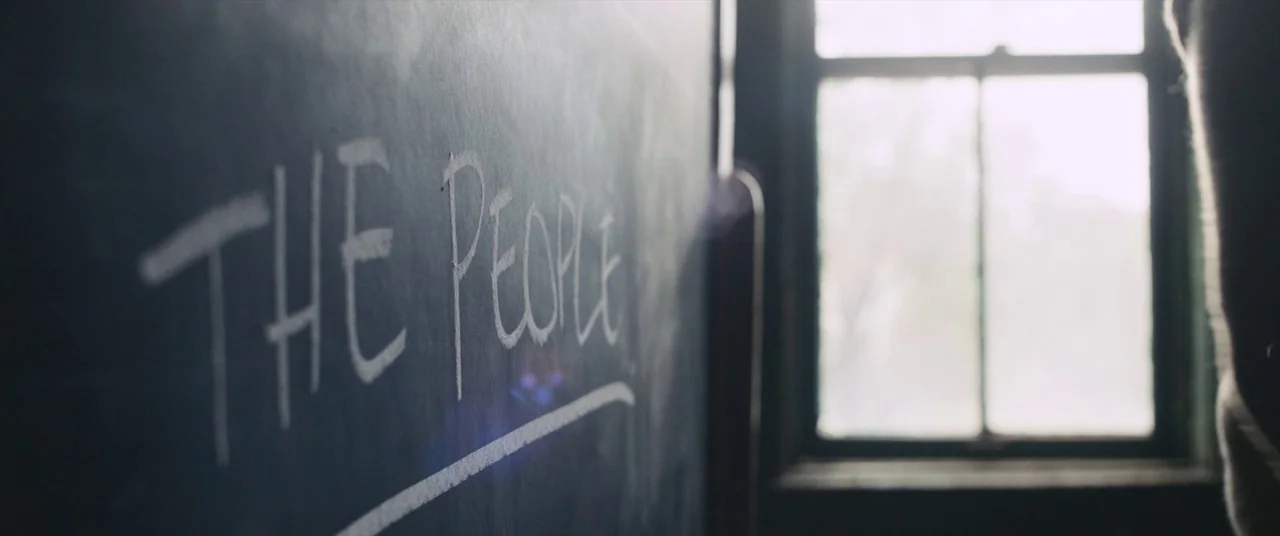Judas and the Black Messiah (2021) movie still: closeup — A dark, worn chalkboard displays handwritten text in white chalk. A bright, out-of-focus…