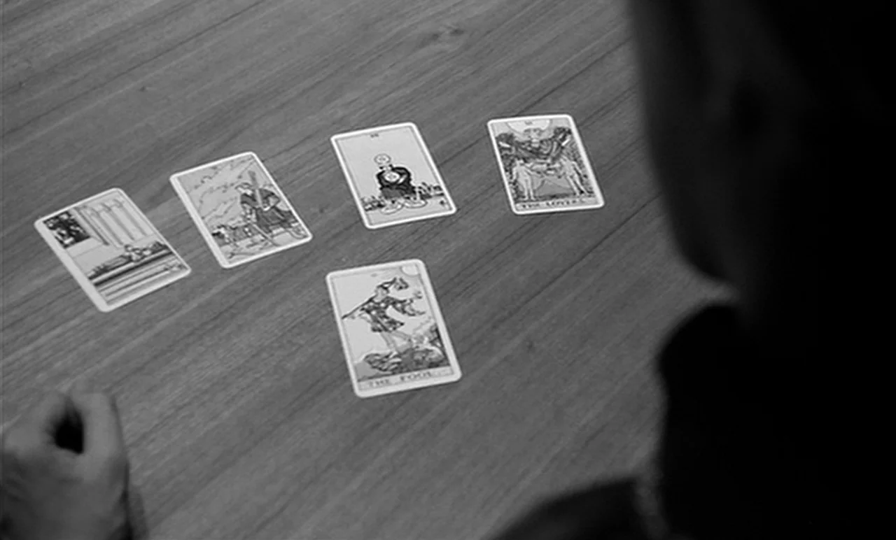 Stereo (1969) movie still: medium — A wooden table surface displays five spread tarot cards in a fan arrangement. A person is seen from behind,…