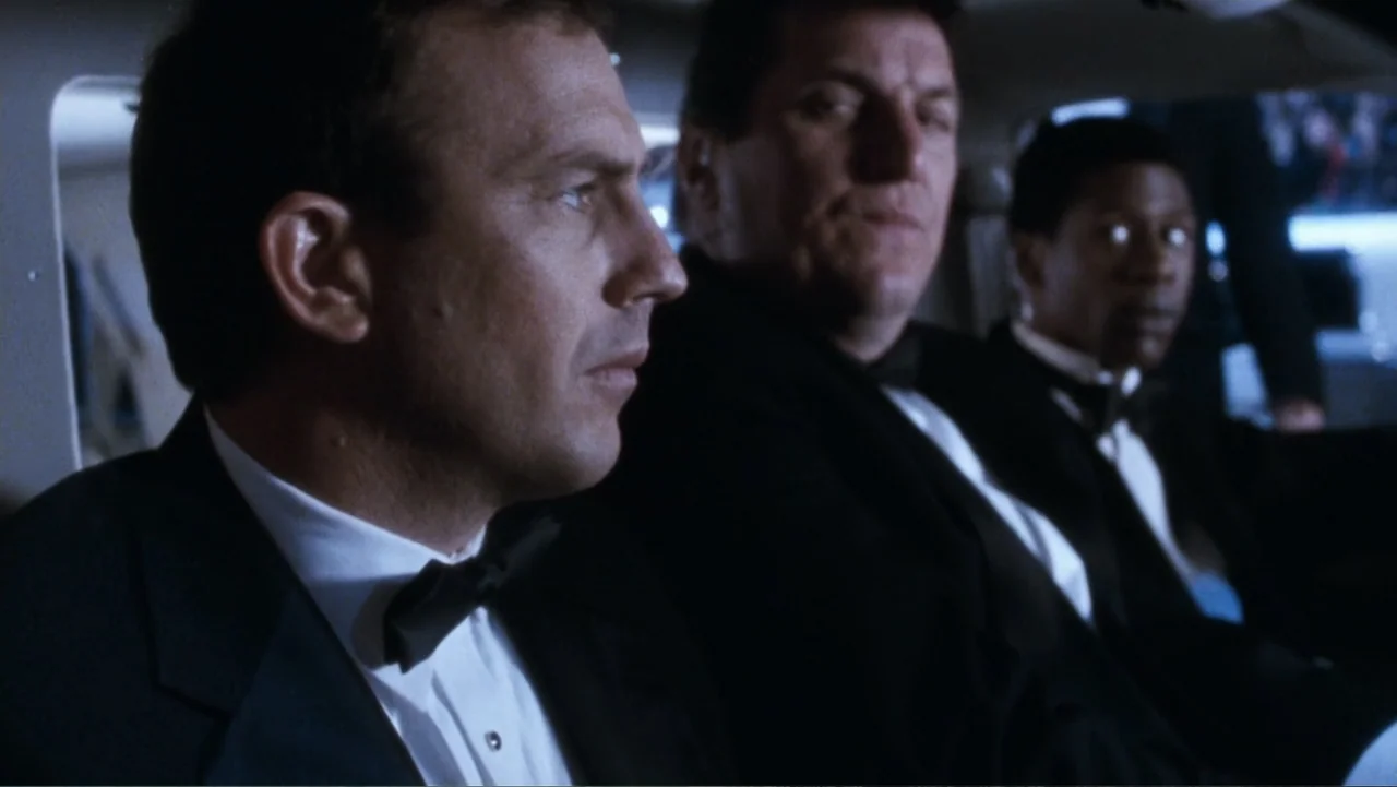 The Bodyguard (1992) movie still: medium — The interior of a limousine at night with three men sitting in a row. They are dressed in formal…