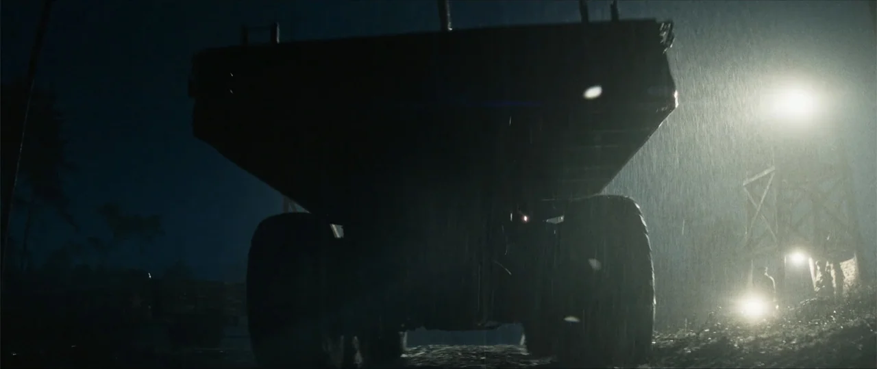 Sisu: Road to Revenge (2025) movie still: fullbody — A massive industrial dump truck dominates a muddy construction site under rainy night…