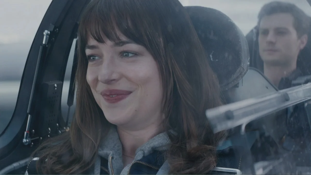 Fifty Shades of Grey (2015) movie still: medium — A view inside a helicopter cockpit with a clear view of the sky outside. A woman in a grey hoodie…