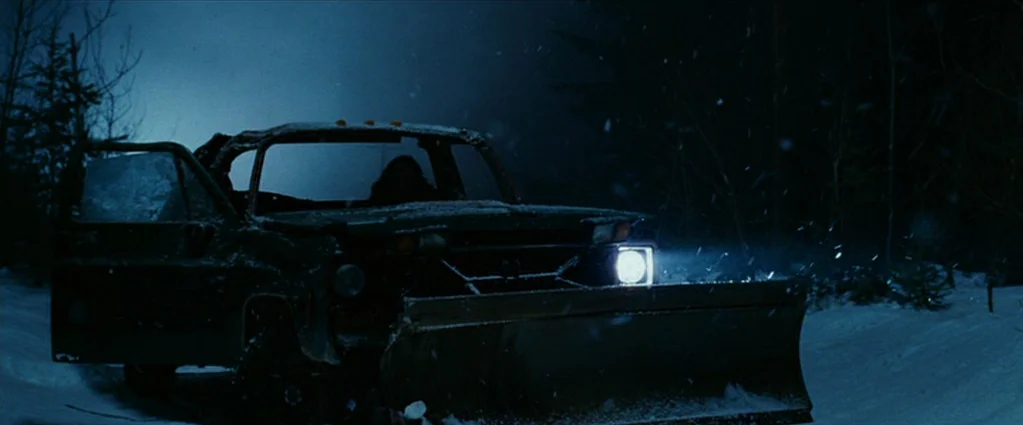 Wind Chill (2007) movie still: wide — A snow-covered clearing in a dark forest contains a damaged truck with a plow. The driver-side door of the…