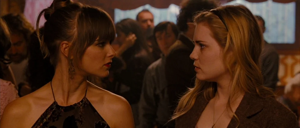 Drag Me to Hell (2009) movie still: medium — A crowded, dimly lit environment features a blurred background of people standing around. Two young…