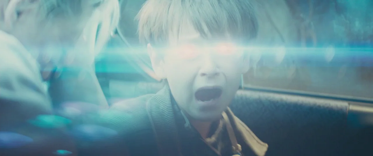 Midnight Special (2016) movie still: closeup — A young boy sits in the dark back seat of a vehicle at night. His eyes emit an intense glowing red…