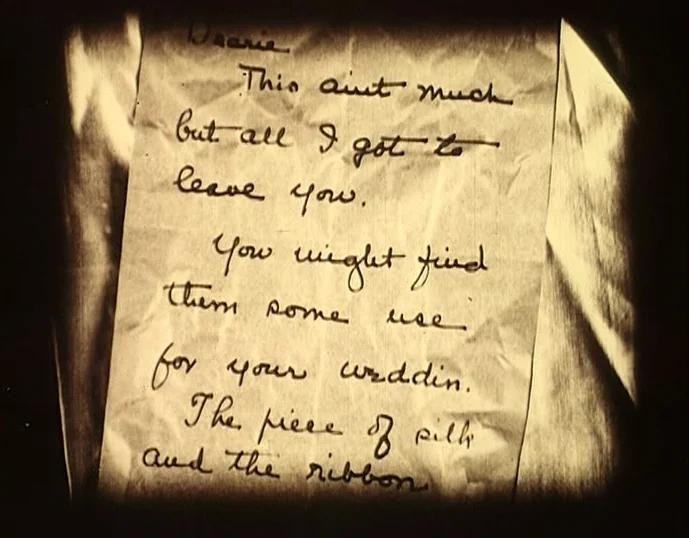 Broken Blossoms (1919) movie still: closeup — A crinkled piece of paper sits centrally in the frame with handwritten cursive text. The handwritten…