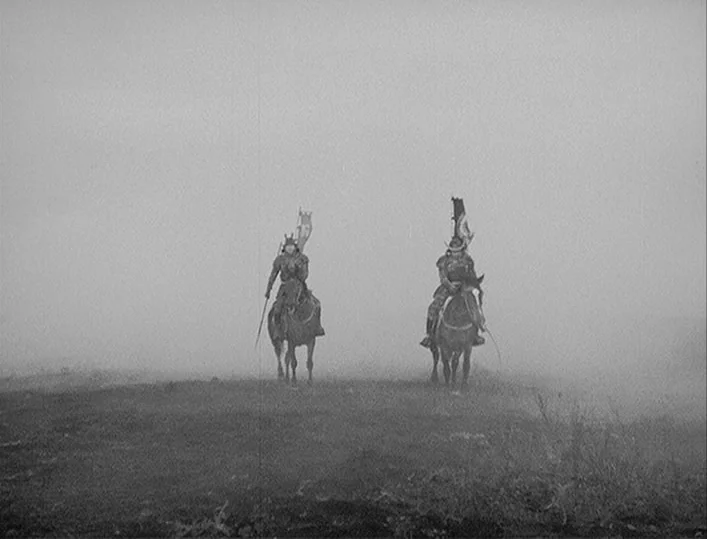 Throne of Blood (1957) movie still: wide — An open field is obscured by a thick layer of low-hanging fog. Two mounted samurai warriors ride towards…