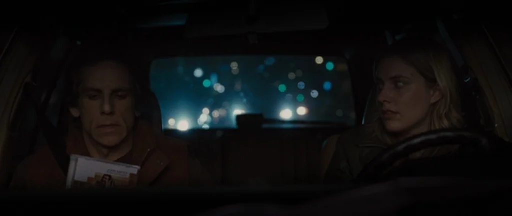 Greenberg (2010) movie still: medium — The interior of a car at night shows a man and woman side by side. Outside the rear windshield, blurred city…