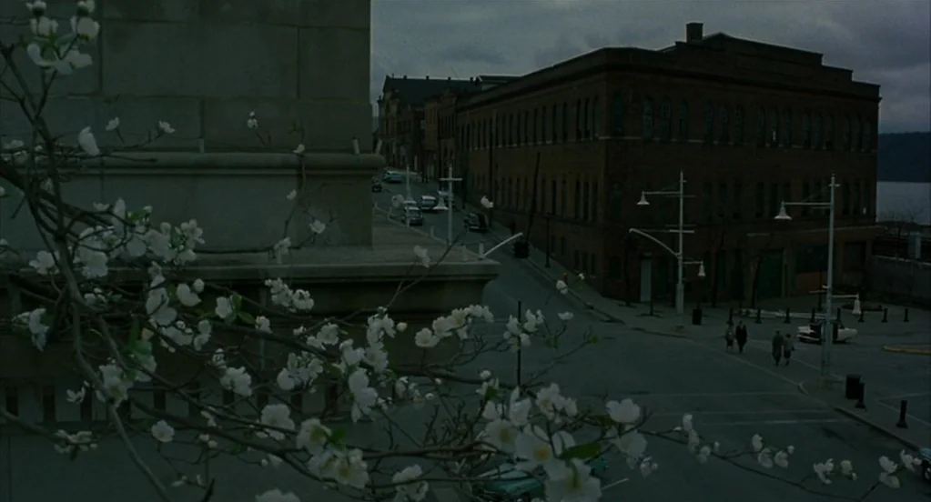 Far From Heaven (2002) movie still: establishing — A quiet town street corner features a large brick factory building under overcast skies. White…