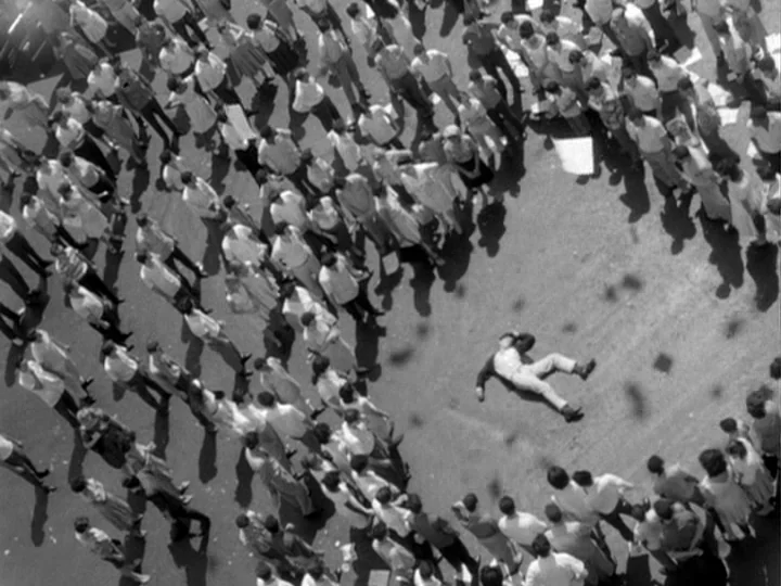 I Am Cuba (1964) movie still: establishing — An expansive outdoor paved area is filled with a dense crowd of standing people. A single person lies…