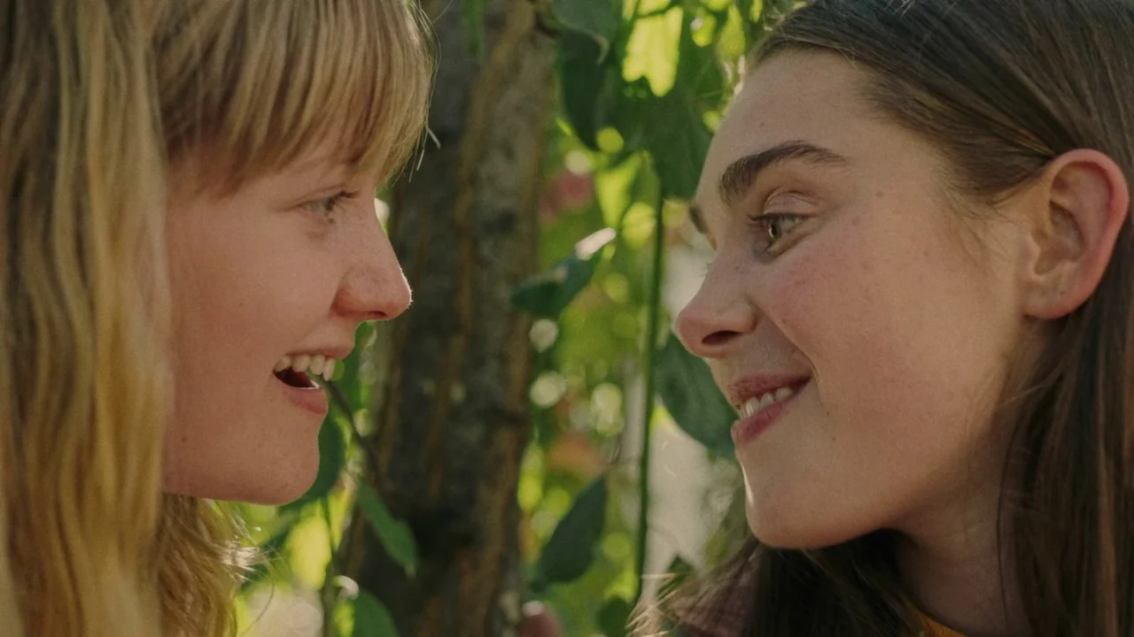 My First Summer (2020) movie still: closeup — Two women stand in a sunlit area filled with dense green leafy plants. The two subjects face each…