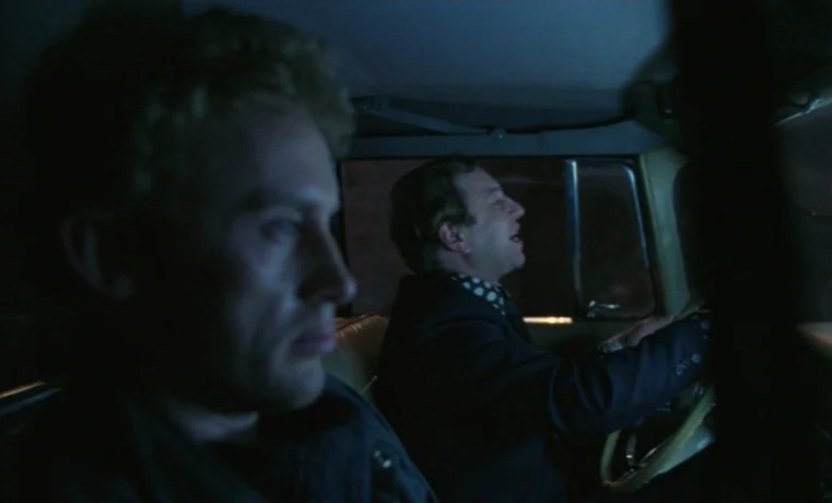 Ga-ga: Glory to the Heroes (1986) movie still: medium — The interior of a car travels through the night with a dark cabin. Two men sit in the front…