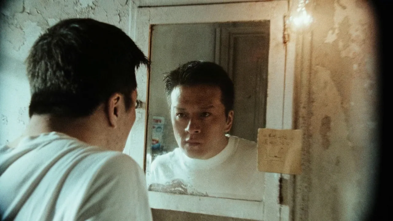 Suzhou River (2000) movie still: medium — A small bathroom has a weathered mirror mounted on a wall with peeling paint. A man looks directly into…