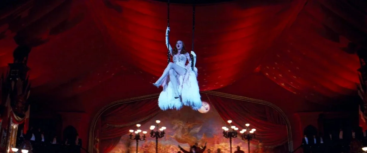 Moulin Rouge! (2001) movie still: wide — A large red theater interior featuring a prominent hanging trapeze structure above the floor. A woman in a…