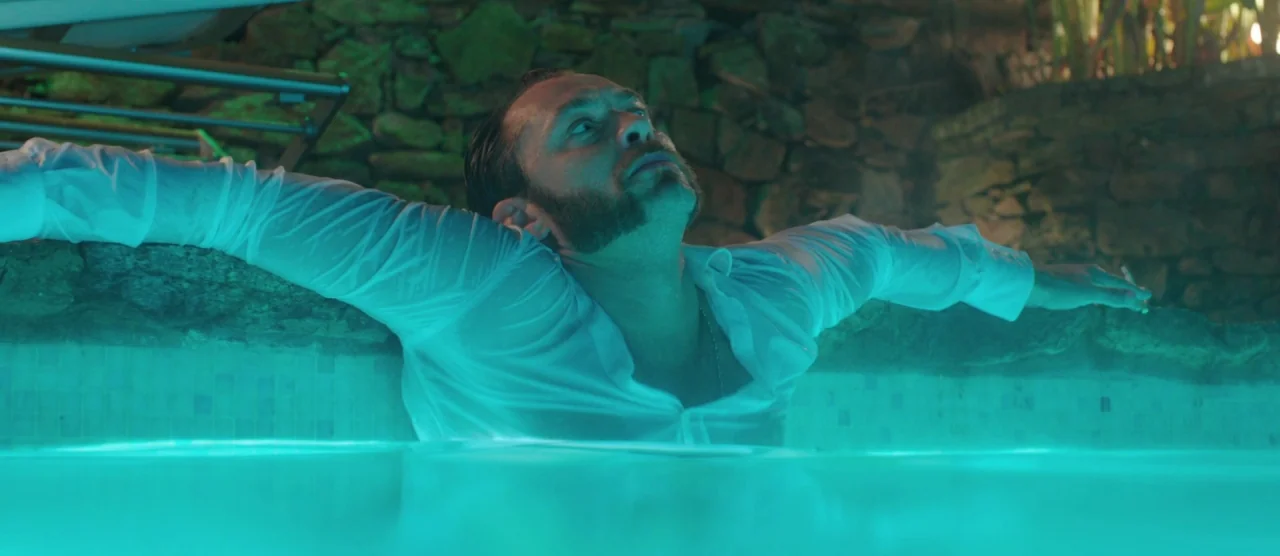 Dom Hemingway (2013) movie still: medium — A man stands in a brightly lit pool at night with a rough stone wall. The water glows with intense…