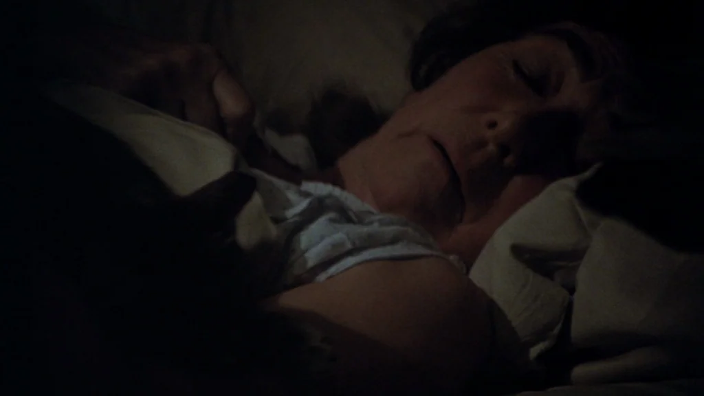 Cabaret (1972) movie still: closeup — A dimly lit room at night with a person sleeping in a bed. The individual rests their head on pillows with…