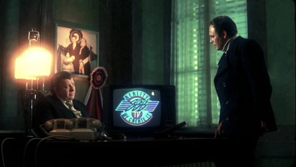 The War of the Worlds: Next Century (1981) movie still: medium — A dimly lit office features a heavy wooden desk, a television, and green-tinted…