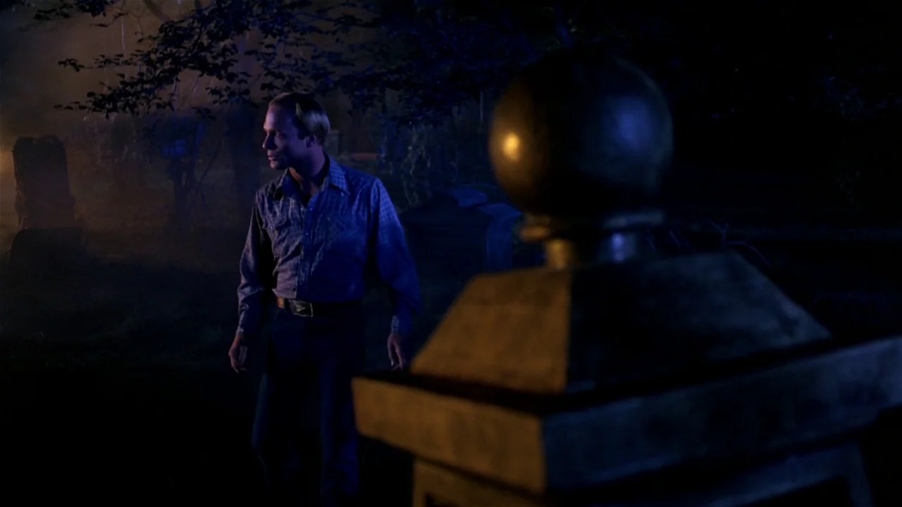 Creepshow (1982) movie still: medium — A nighttime cemetery features dark gravestones and trees partially obscured by heavy blue fog. A man in a…