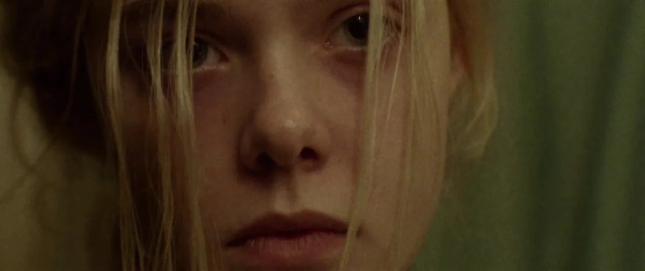 Low Down (2014) movie still: closeup — A close-up of a young woman's face against a dark, muted olive background. The subject stares straight at the…