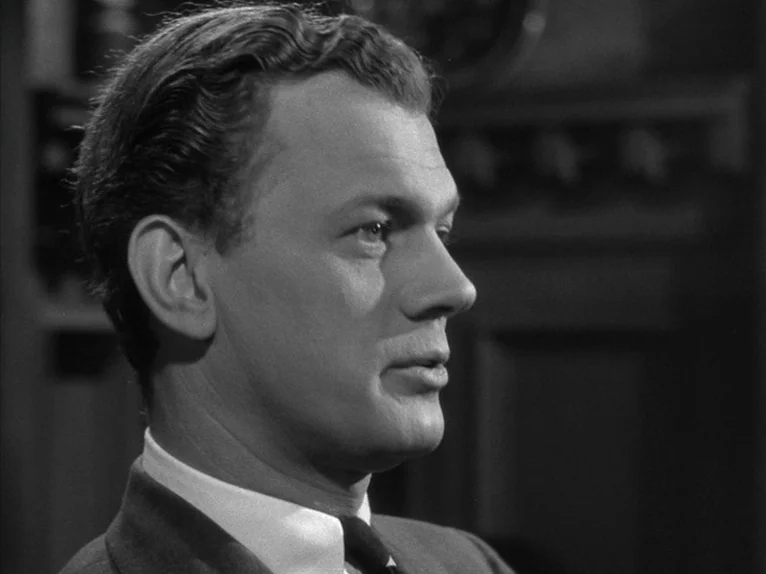 Shadow of a Doubt (1943) movie still: closeup — An interior space with wood paneled walls dimly visible in the soft background. A man in a suit…