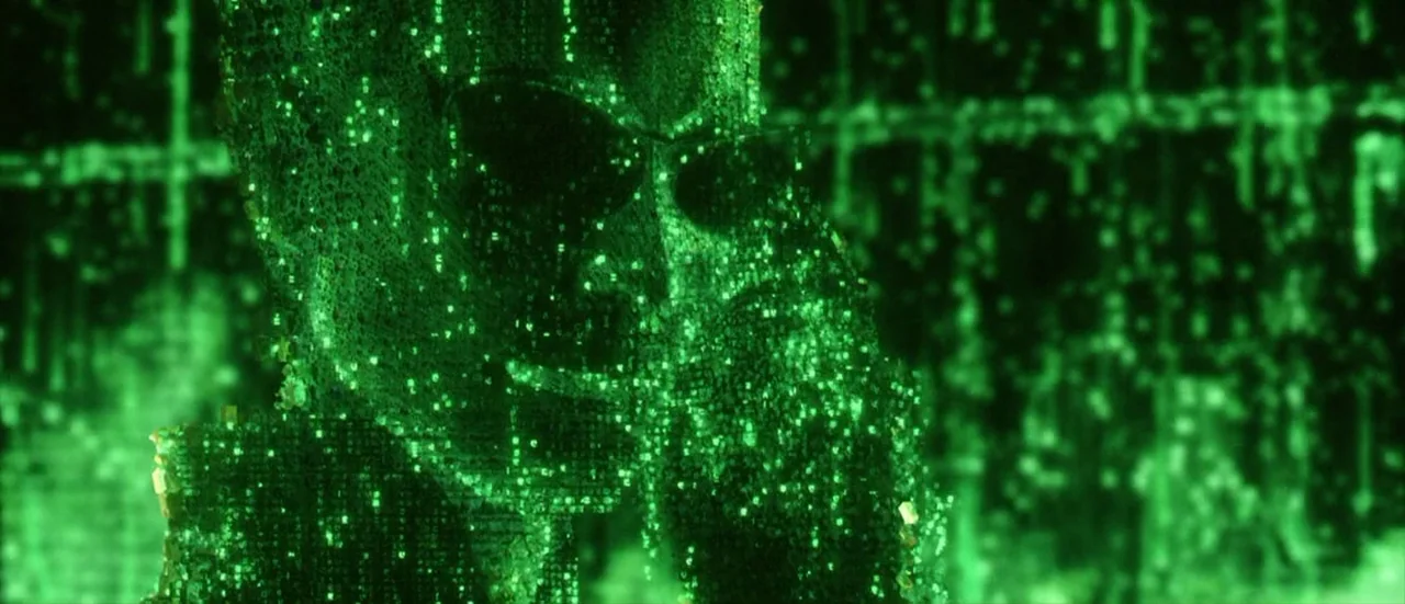 The Matrix Reloaded (2003) movie still: closeup — A man's silhouette is composed of bright green digital code against a black background. The figure…