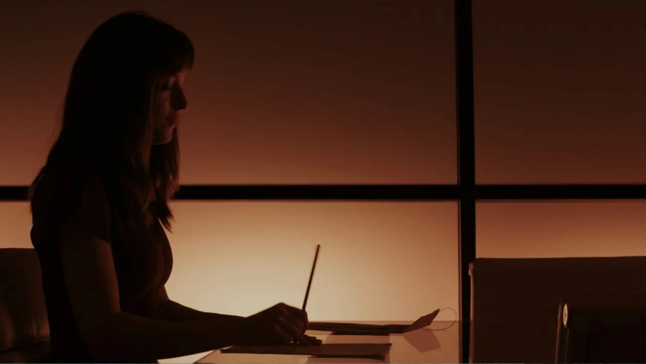 Fifty Shades of Grey (2015) movie still: medium — An interior office space features a large window with warm diffused evening light. A woman in…