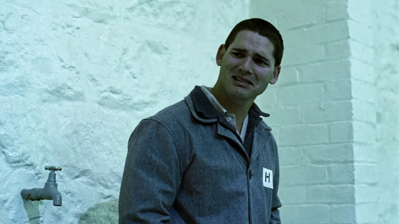 Chopper (2000) movie still: medium — A stark room with painted white brick walls and an industrial metal water tap. A man in a grey work jacket…