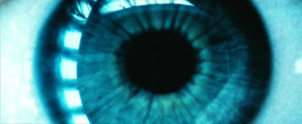 Minority Report movie still: closeup — A close-up view of a human eye with sharp focus on the iris. Light reflections from a grid-like source are…