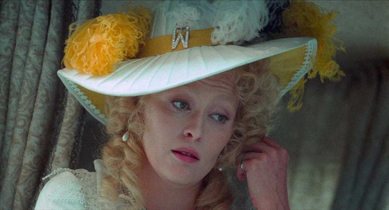 The Three Musketeers (1973) movie still: closeup — A woman sits inside an ornate carriage with patterned upholstery and fabric curtains. She wears a…