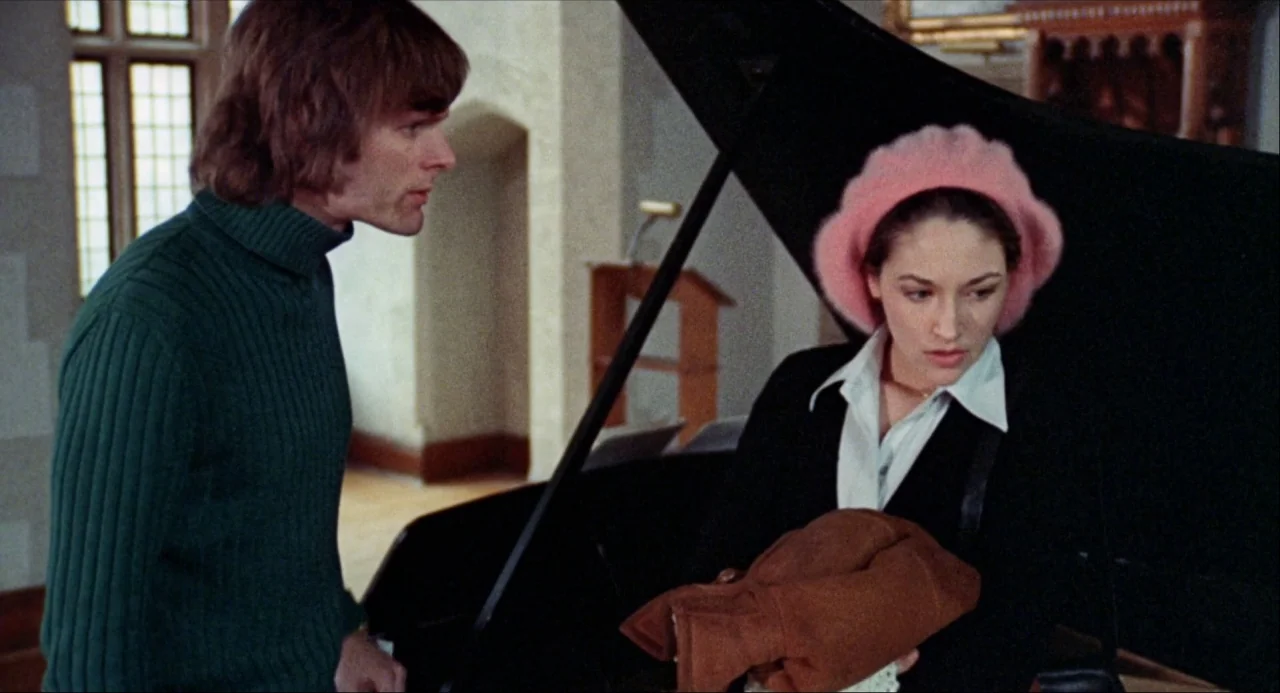 Black Christmas (1974) movie still: medium — A stone-walled interior room contains a large open black grand piano and wooden furniture. A man in a…