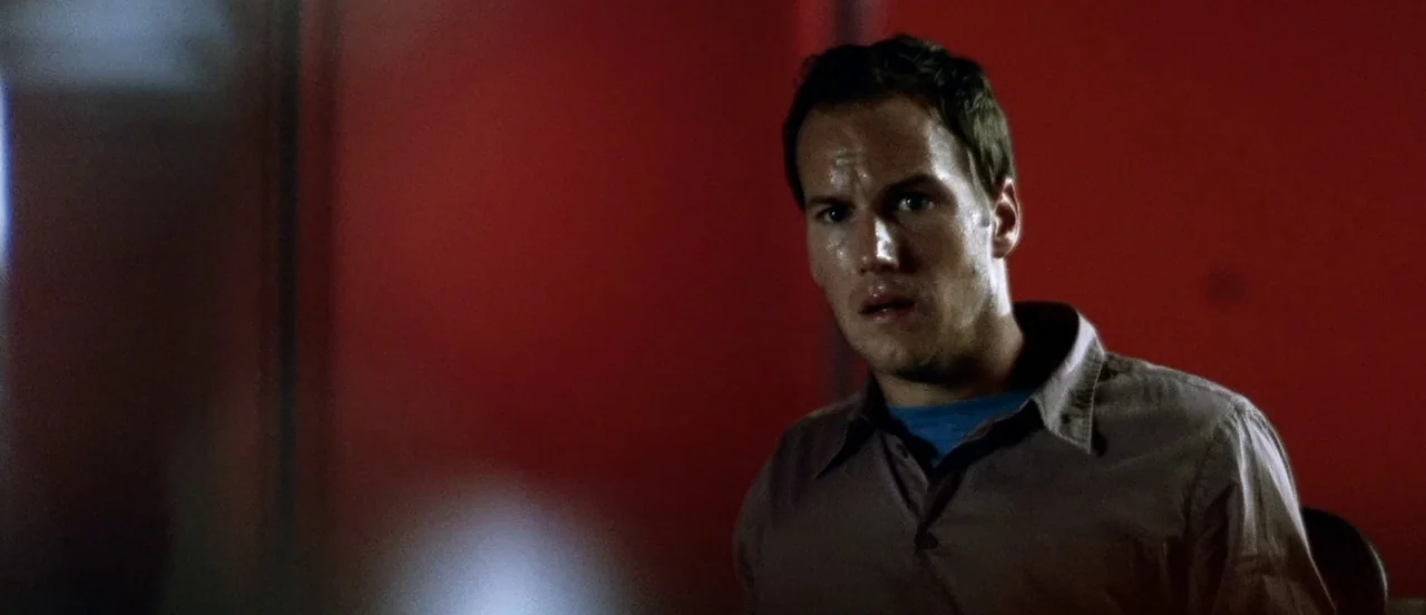 Hard Candy (2005) movie still: medium — A man stands before a flat, solid dark red wall in a dim room. He looks directly toward the camera with an…