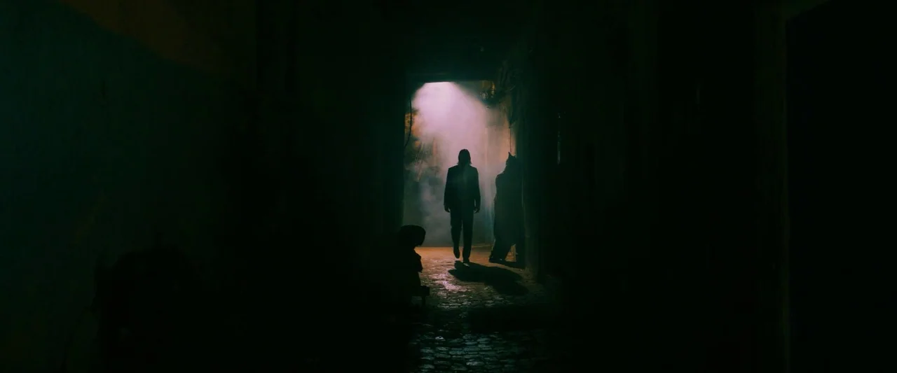 John Wick: Chapter 3 – Parabellum (2019) movie still: wide — A dark narrow stone alleyway is filled with dense clouds of smoke and haze. A man in a…