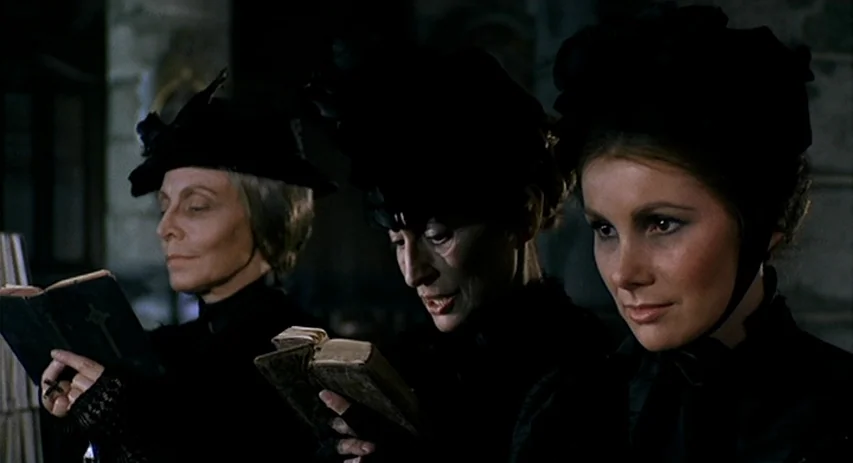 Malpertuis (1971) movie still: medium — Three women in black mourning attire sit in a dark, stone-walled religious interior. Each woman holds a…