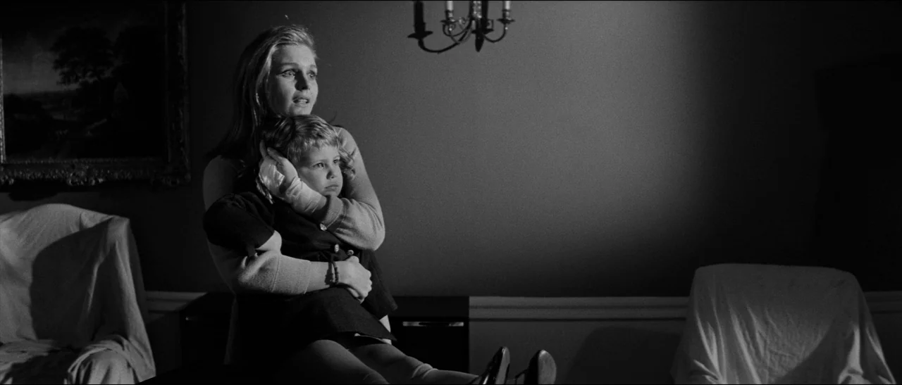 Bunny Lake Is Missing (1965) movie still: medium — A dimly lit room contains draped furniture and a dark wall with a chandelier. A woman clutches a…