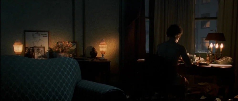Confessions of a Dangerous Mind (2002) movie still: wide — A dark, dimly lit 1970s living room features vintage patterned furniture and warm table…