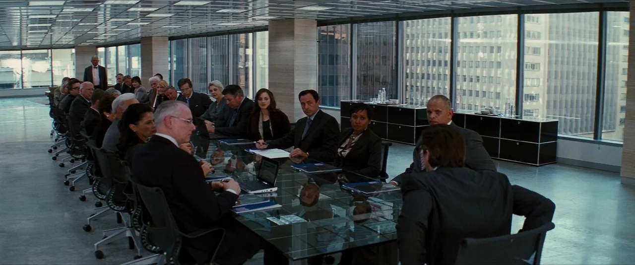 The Dark Knight Rises (2012) movie still: wide — A high-rise glass conference room overlooks a dense city skyline of tall buildings. A group of…