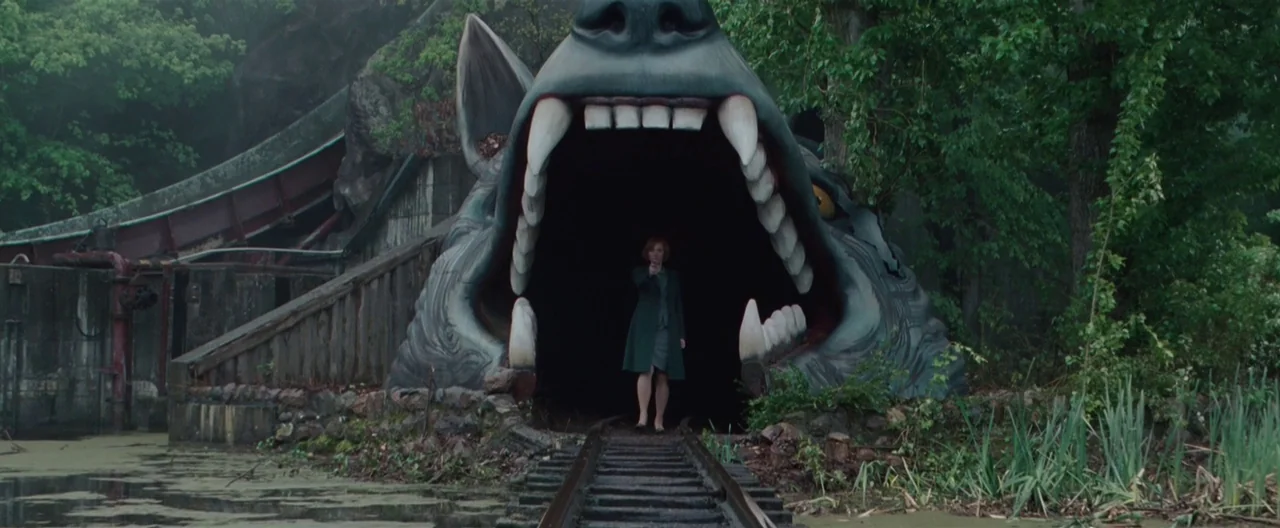 Hanna (2011) movie still: wide — An abandoned amusement park attraction features a massive wolf head acting as a tunnel. A woman stands in the dark…
