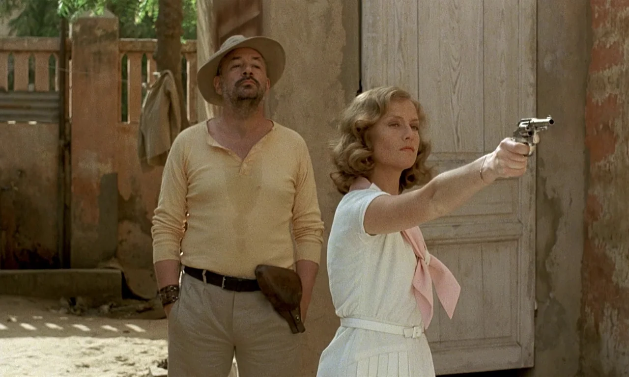 Coup De Torchon (1981) movie still: medium — A sunlit outdoor courtyard features aged walls and a closed wooden door. A woman holds a handgun…
