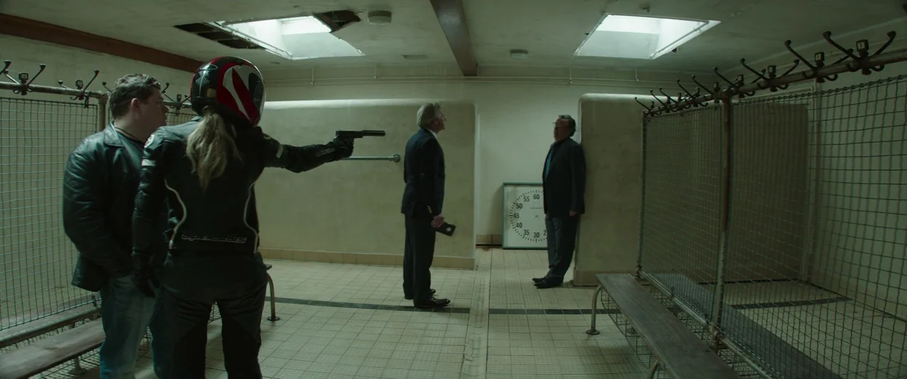 Mindhorn (2016) movie still: fullbody — A utilitarian locker room features tiled walls, metal bench seating, and grid-wire lockers. A person holds a…