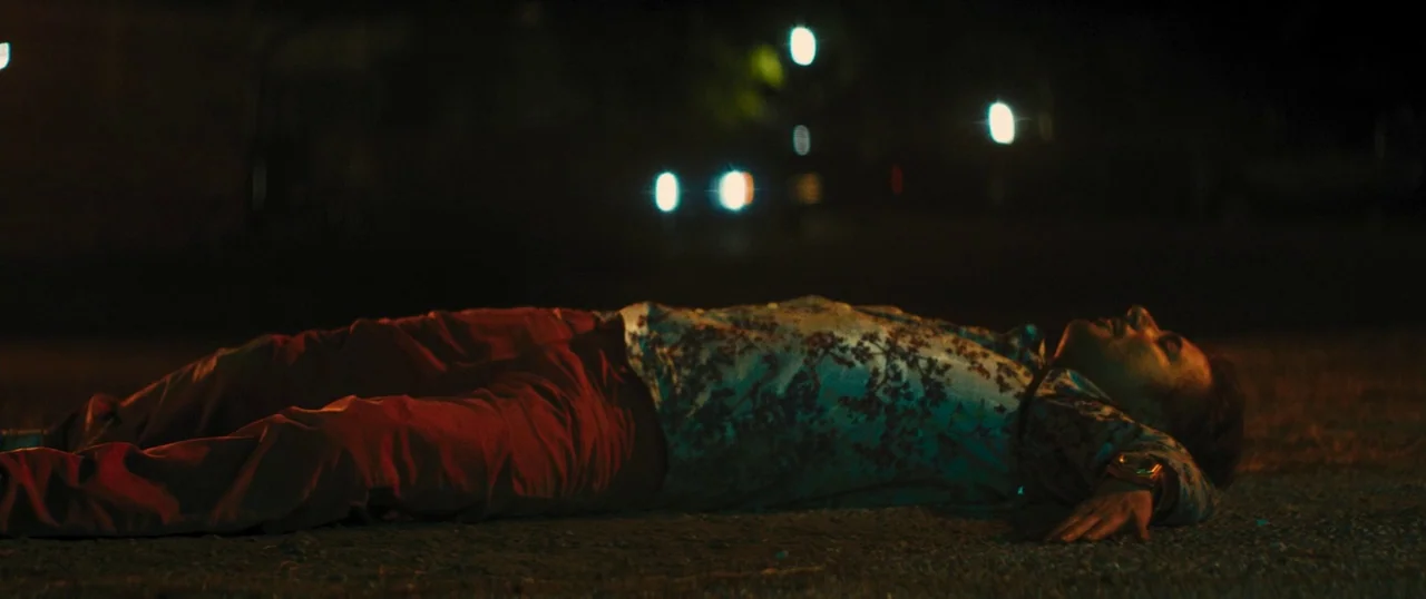 Manglehorn (2014) movie still: fullbody — A person lies prone on dark asphalt at night under the glow of streetlights. The figure rests with arms…