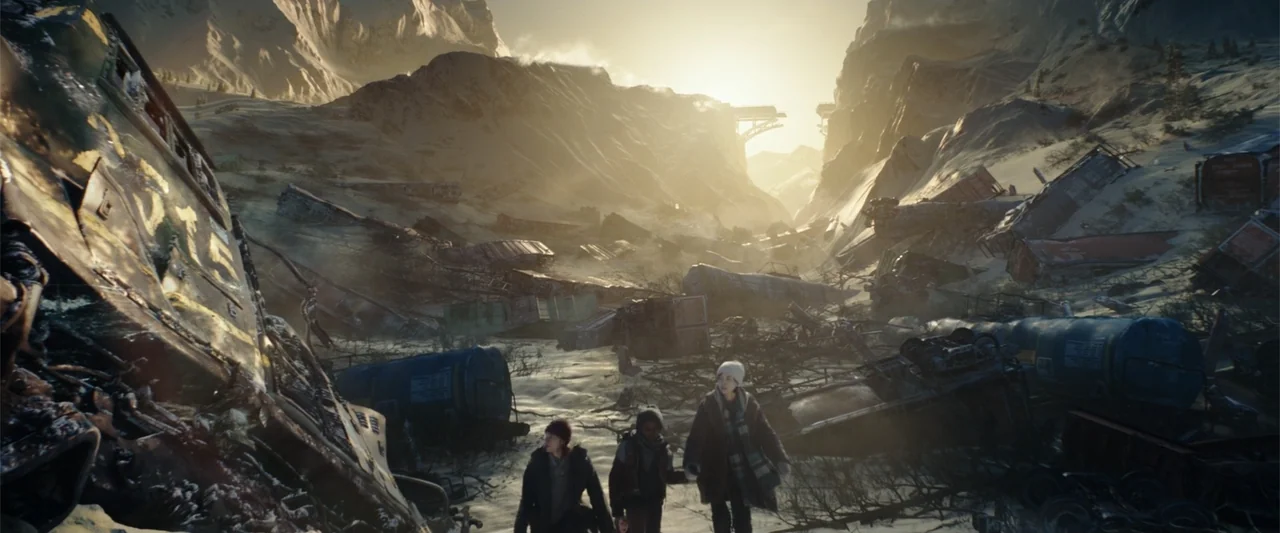 Moonfall (2022) movie still: wide — A snow-covered mountain pass is littered with wreckage from numerous crashed train cars. Three people walk…
