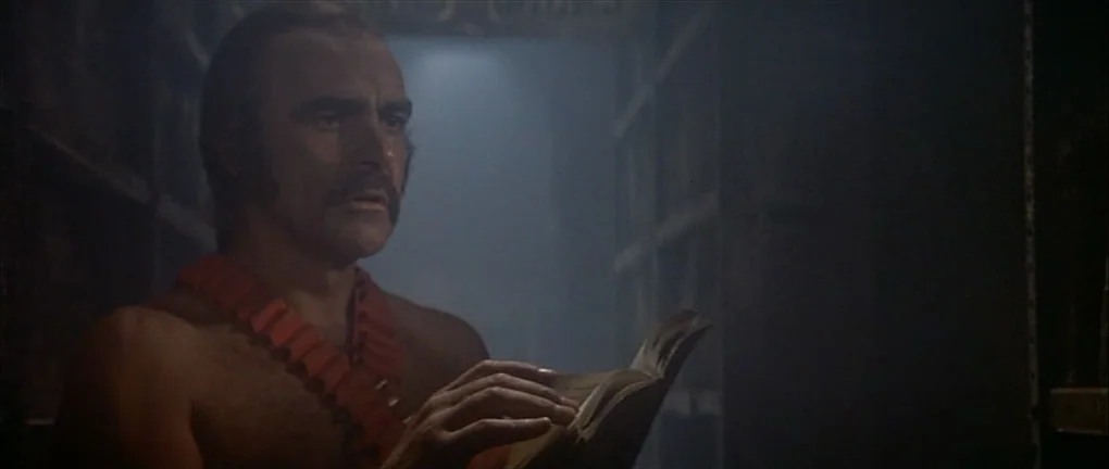 Zardoz (1974) movie still: medium — A dimly lit room filled with tall shelves of books in a haze of smoke. A bare-chested man wearing a red…