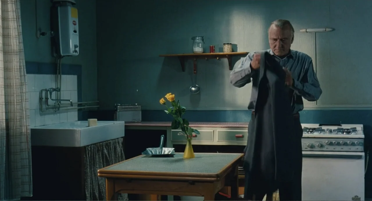 Le Havre (2011) movie still: medium — A utilitarian kitchen features a tiled counter with a sink and a central table. An elderly man stands near the…
