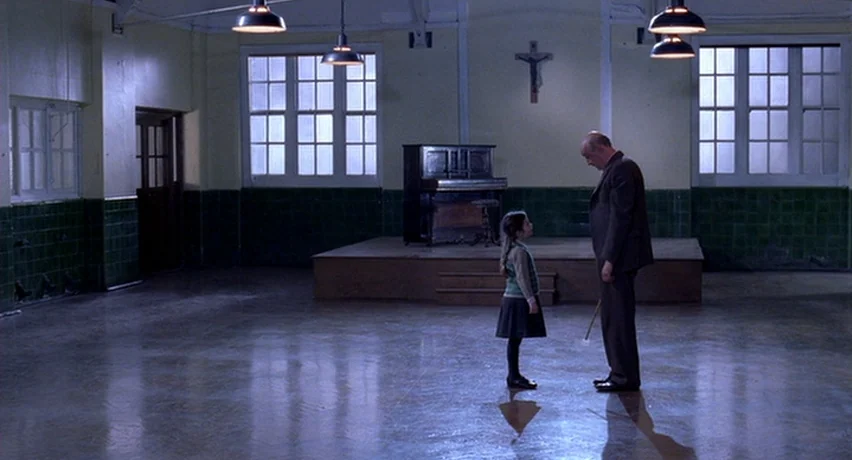 The Man Who Cried (2000) movie still: wide — A sparse school assembly hall features green tiled walls and a wooden stage.